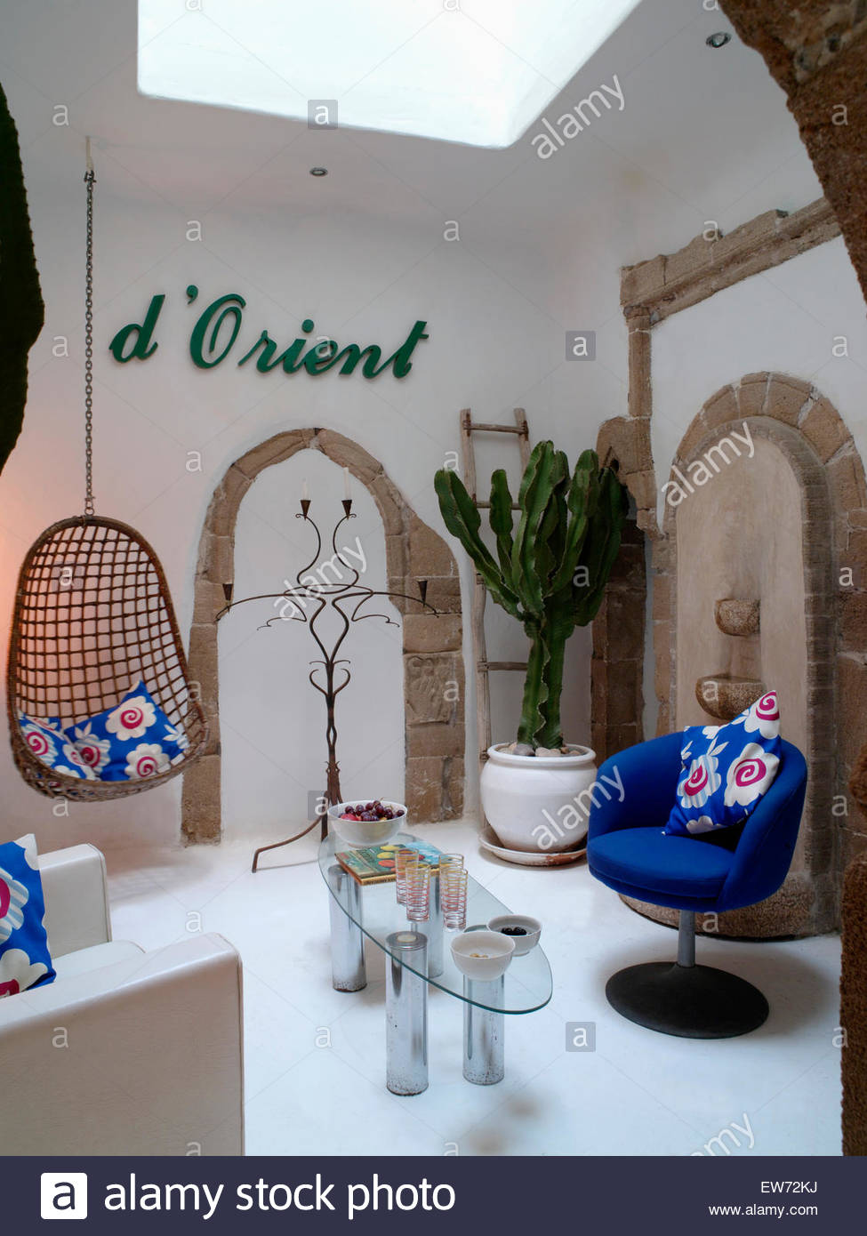 balancoire et grand cactus dans salon marocain avec table basse en verre et bleu fauteuil avec coussins colores ew72kj