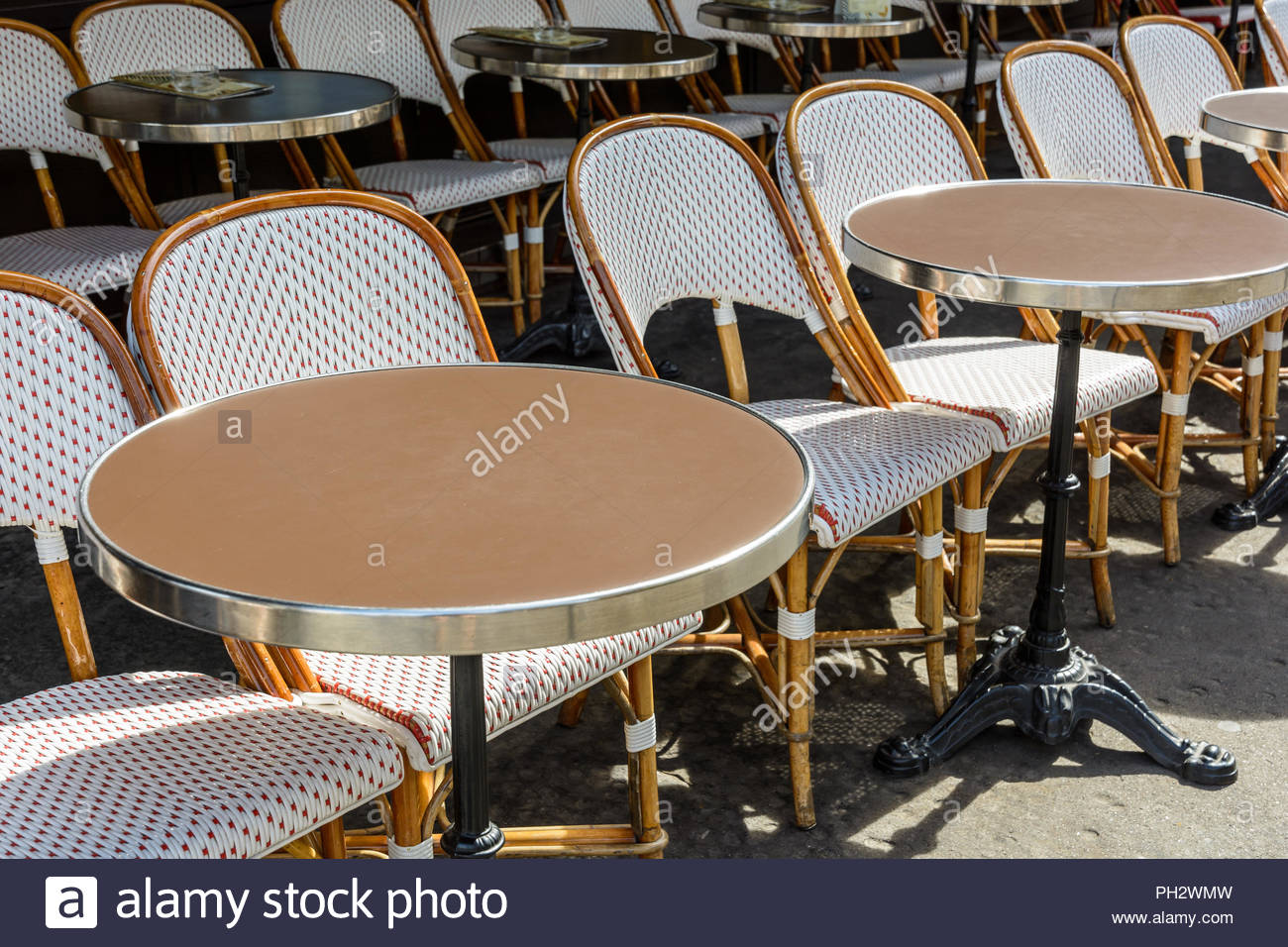 une terrasse typique a l exterieur d une brasserie parisienne mis en place avec des chaises en rotin et des petites tables rondes avec une jambe de fer de fonte ph2wmw